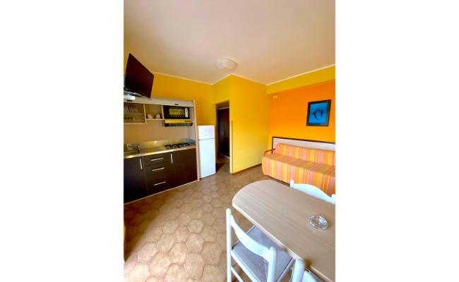 Cucina aperta con mobili scuri, divano a righe colorate e pareti gialle.